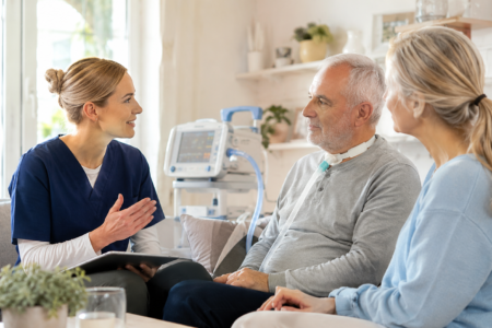 Pflegekraft berät einen Patienten mit Beatmung und eine Angehörige zur ambulanten Intensivpflege im häuslichen Umfeld.